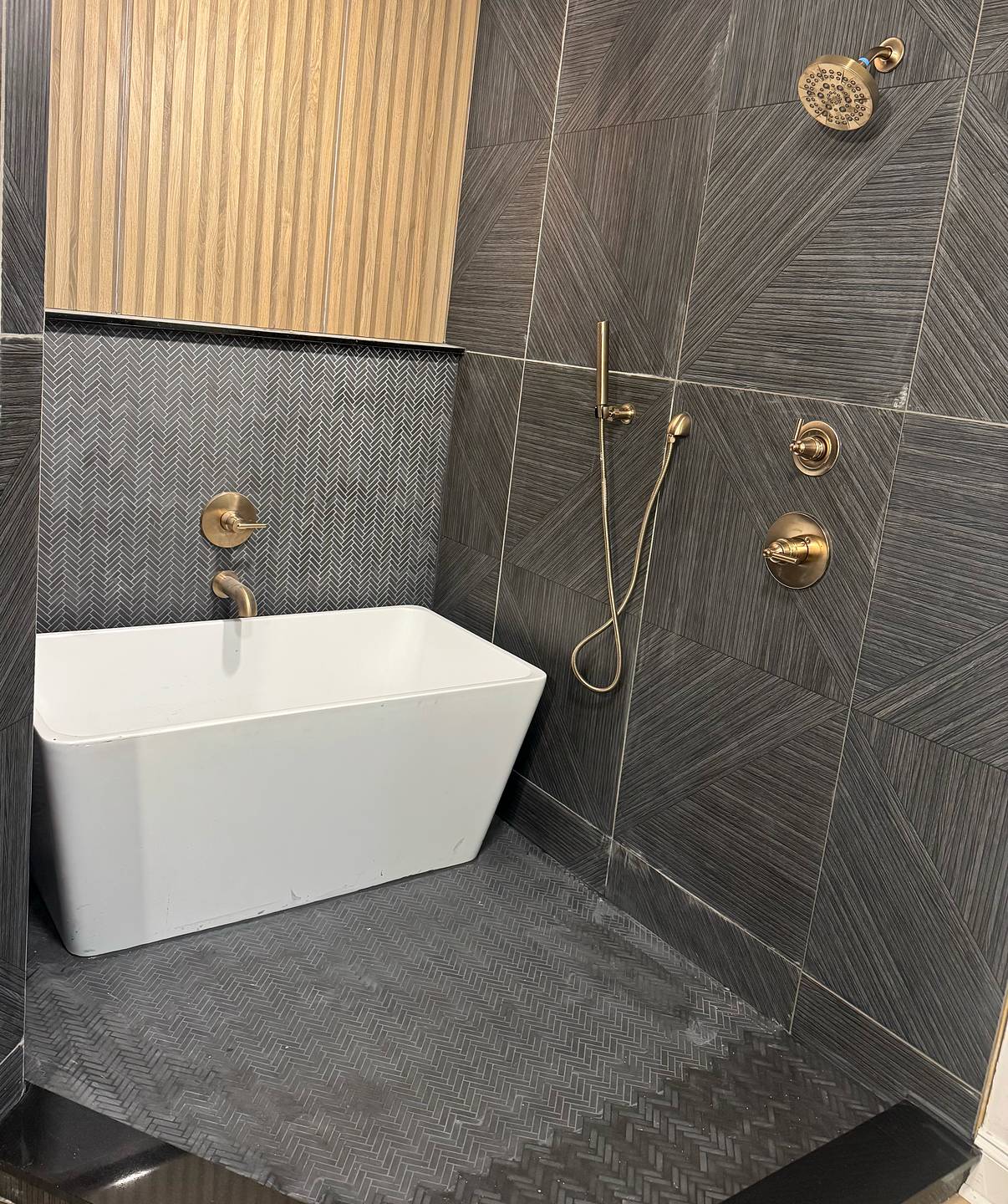 Charcoal tile shower with herringbone mosaic, freestanding tub and brushed brass fixtures