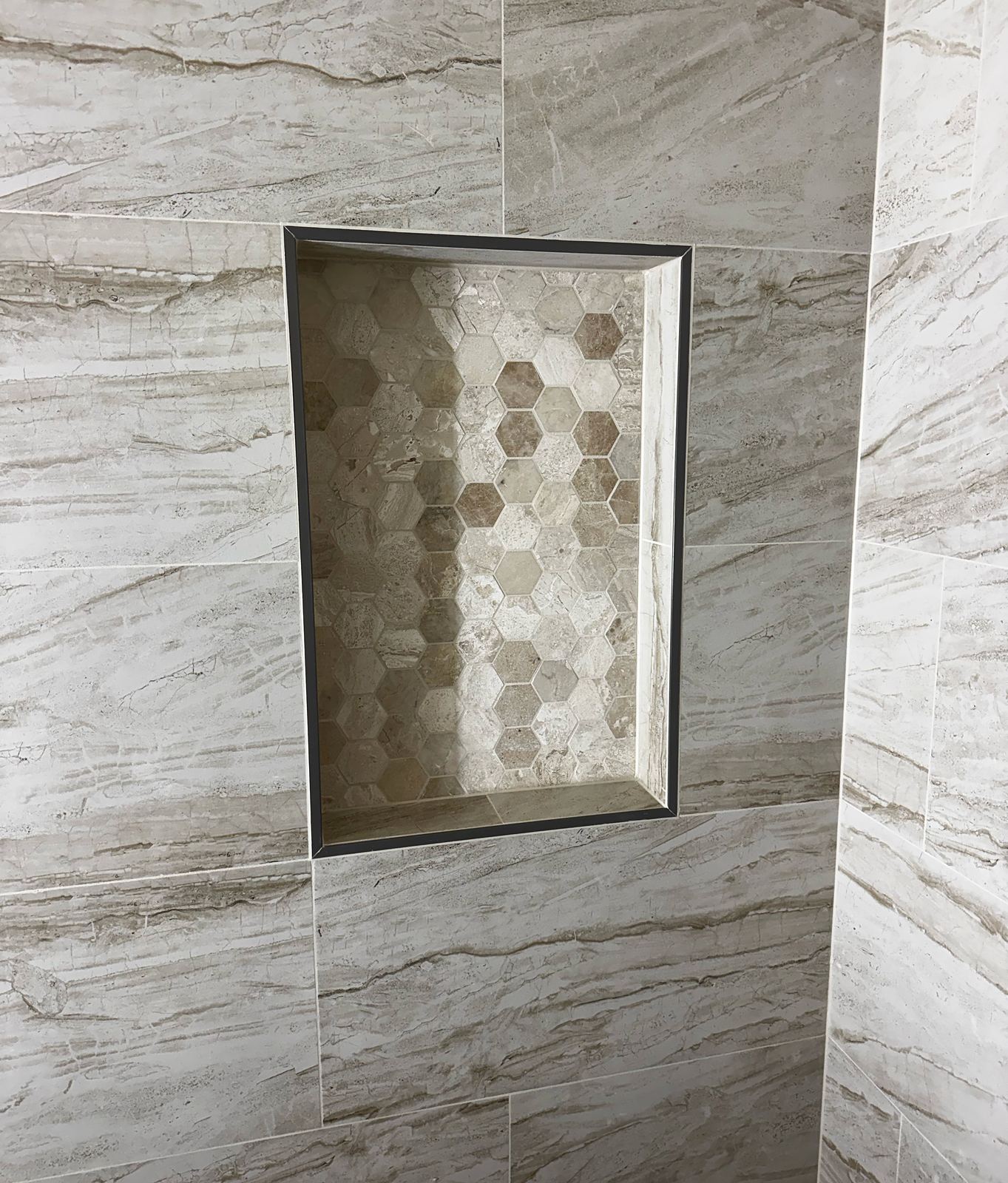 Recessed shower niche with hexagon mosaic tile and dark metal edge trim