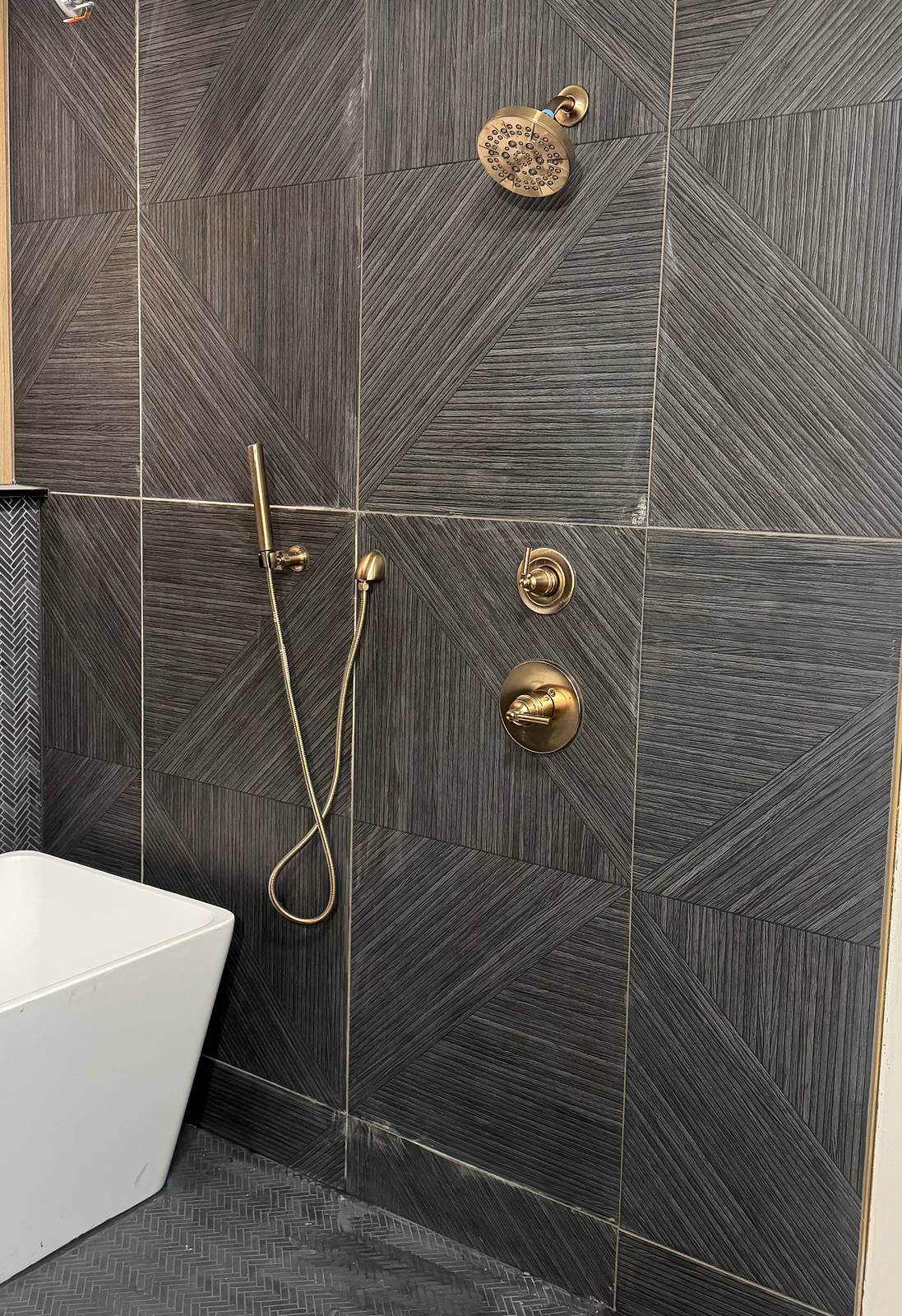 Large-format charcoal tile shower wall with brass shower fixtures